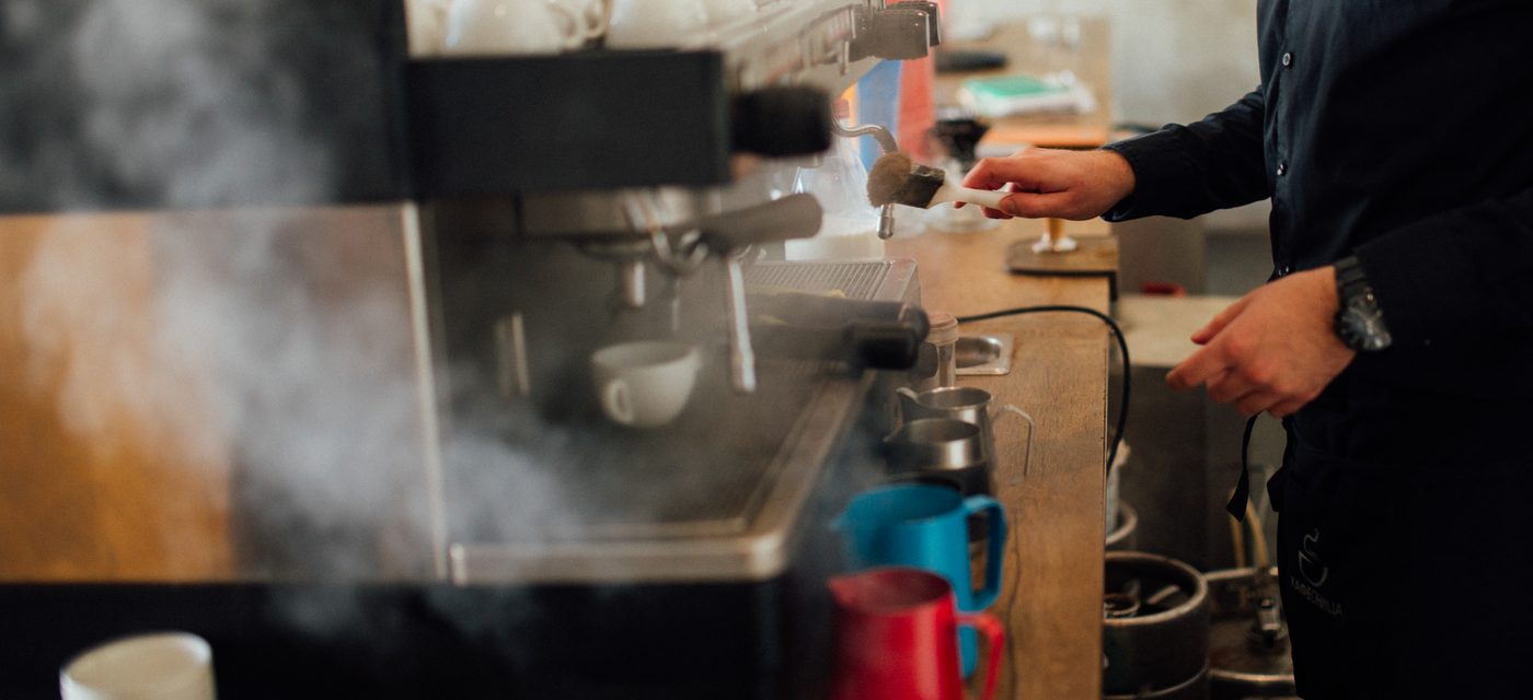 Barista arbetar vid espressomaskin med ånga och mjölkkannor